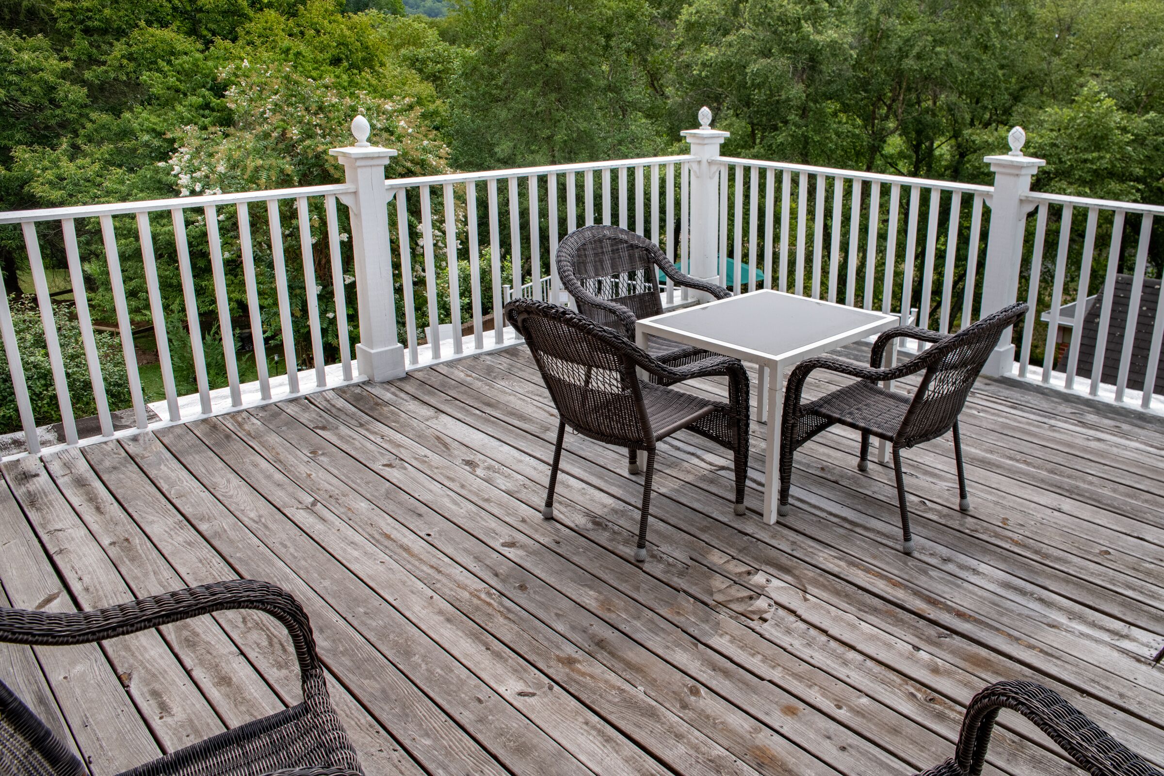 Eine Holzterrasse mit weißer Geländer, zwei Korbstühle und ein kleiner Tisch.