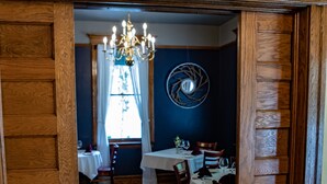 Un couloir aux murs lambrissés mène à une salle à manger agrémentée d’un lustre, d’une table avec des chaises et d’un élément décoratif mural.
