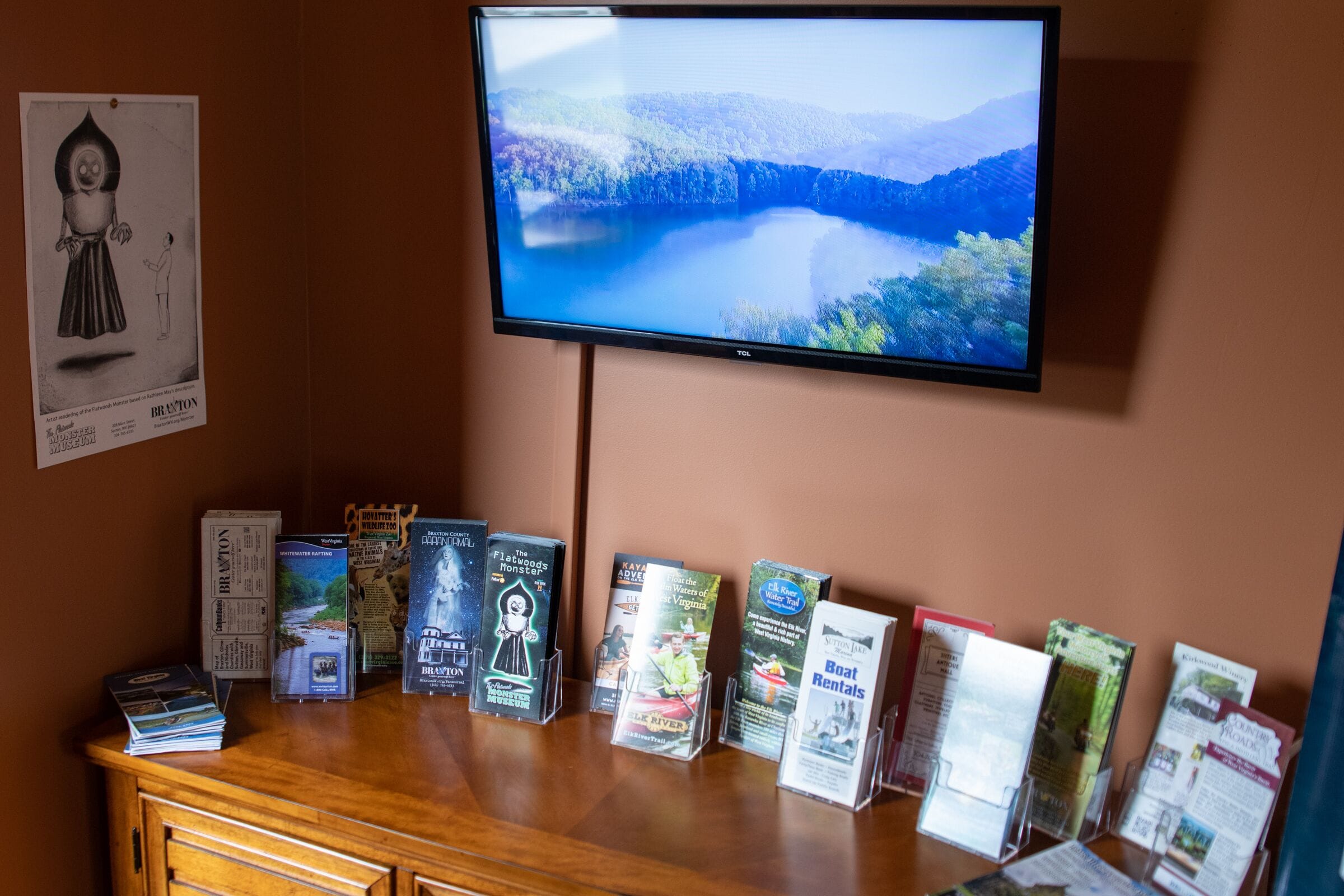 A display of travel brochures and a television screen above a wooden counter.