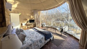 Une pièce confortable avec un lit, un bureau, une télévision et une vue sur l’extérieur grâce à de grandes fenêtres.