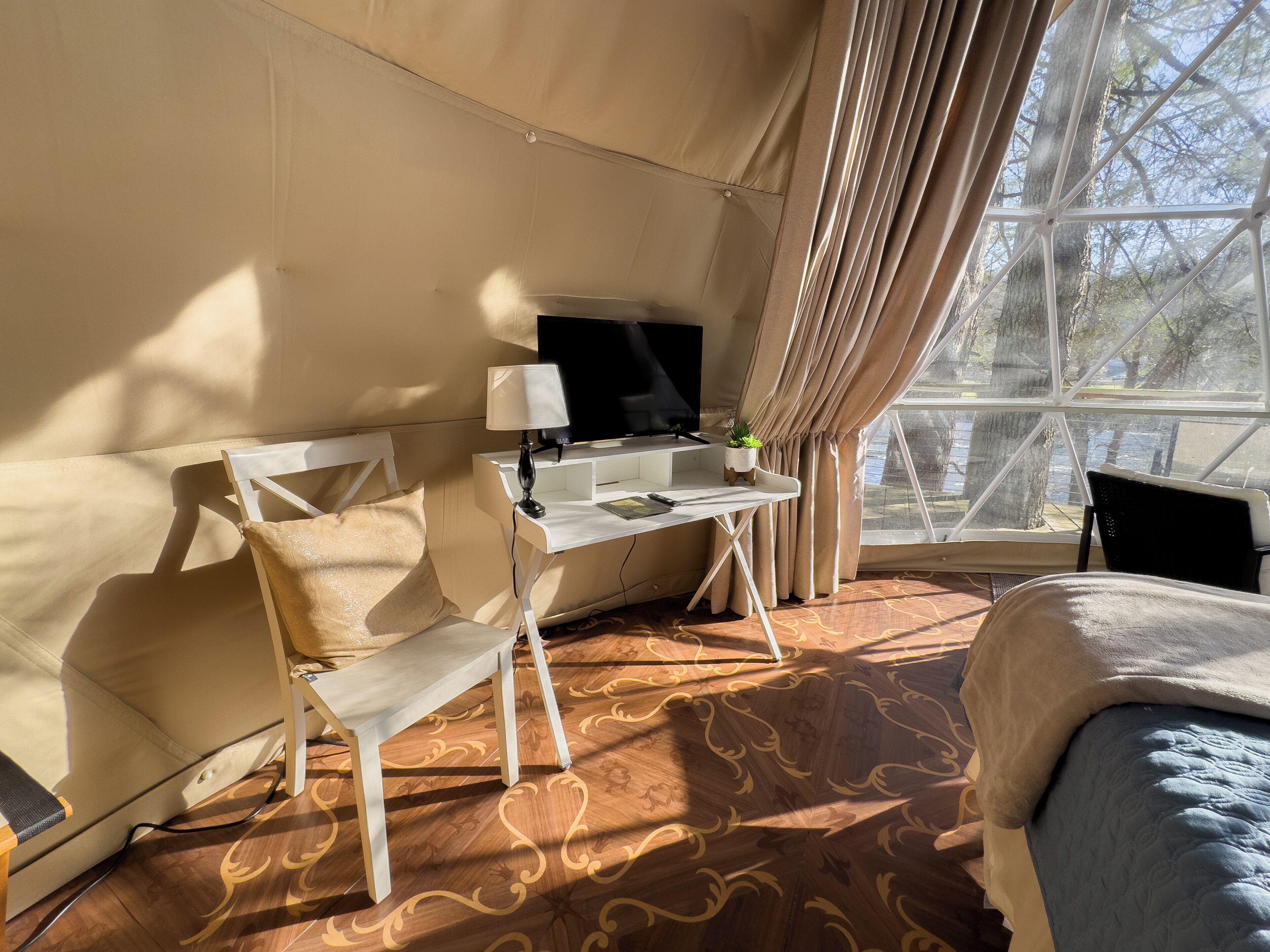 A room with a bed, a desk with a TV, a chair, and a window with curtains.