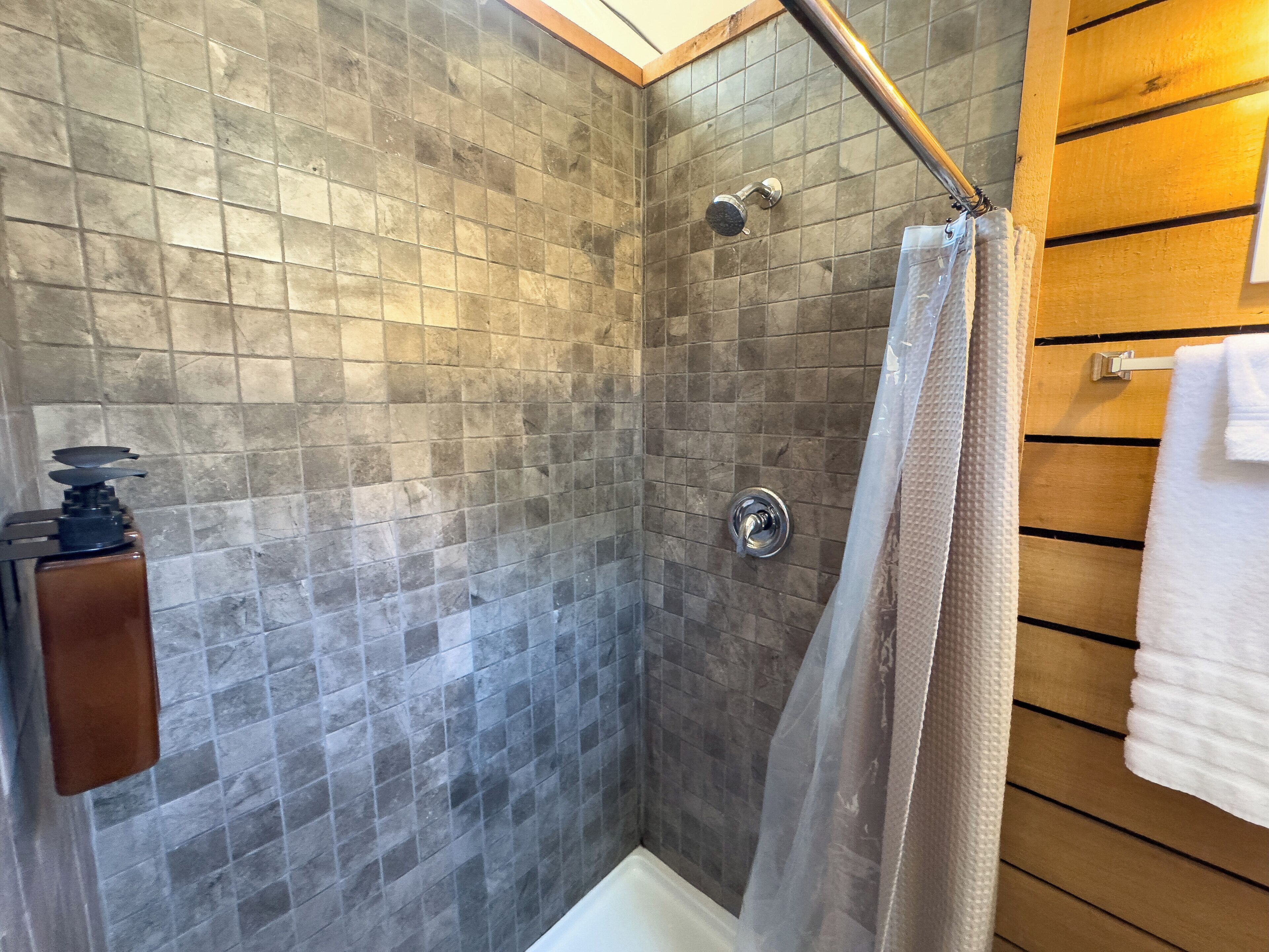 A shower with a glass door, tiled walls, and a wooden panel wall.