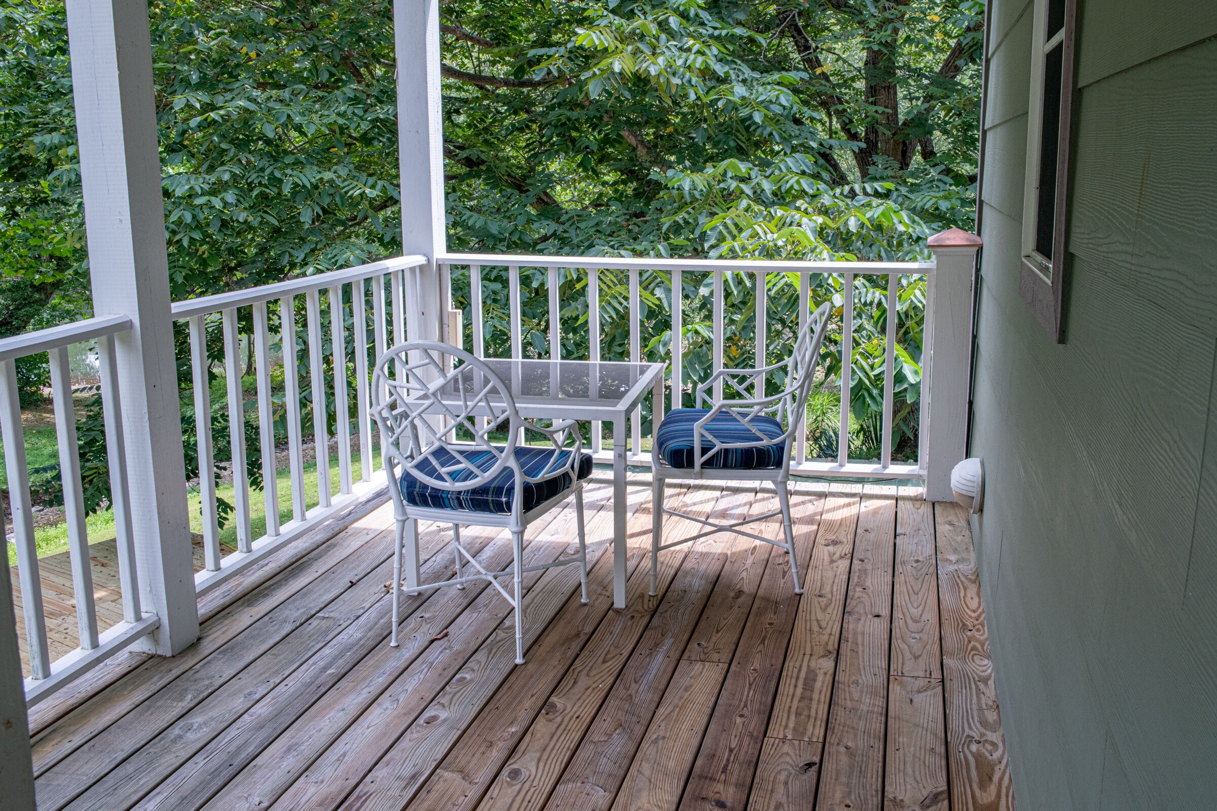 A wooden deck with two white metal chairs and a glass table.
