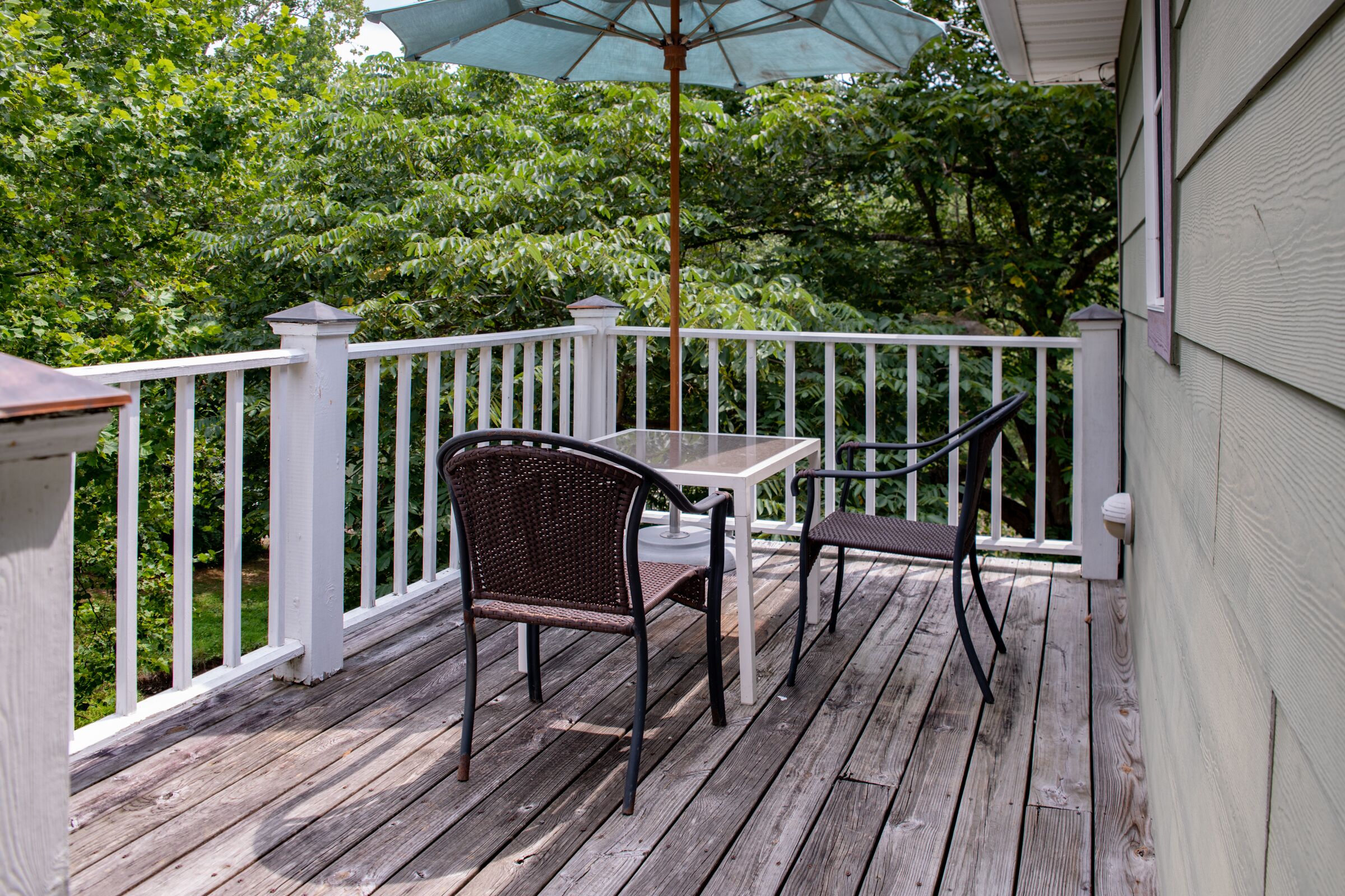 A wooden deck with a table and chairs, surrounded by white railings.