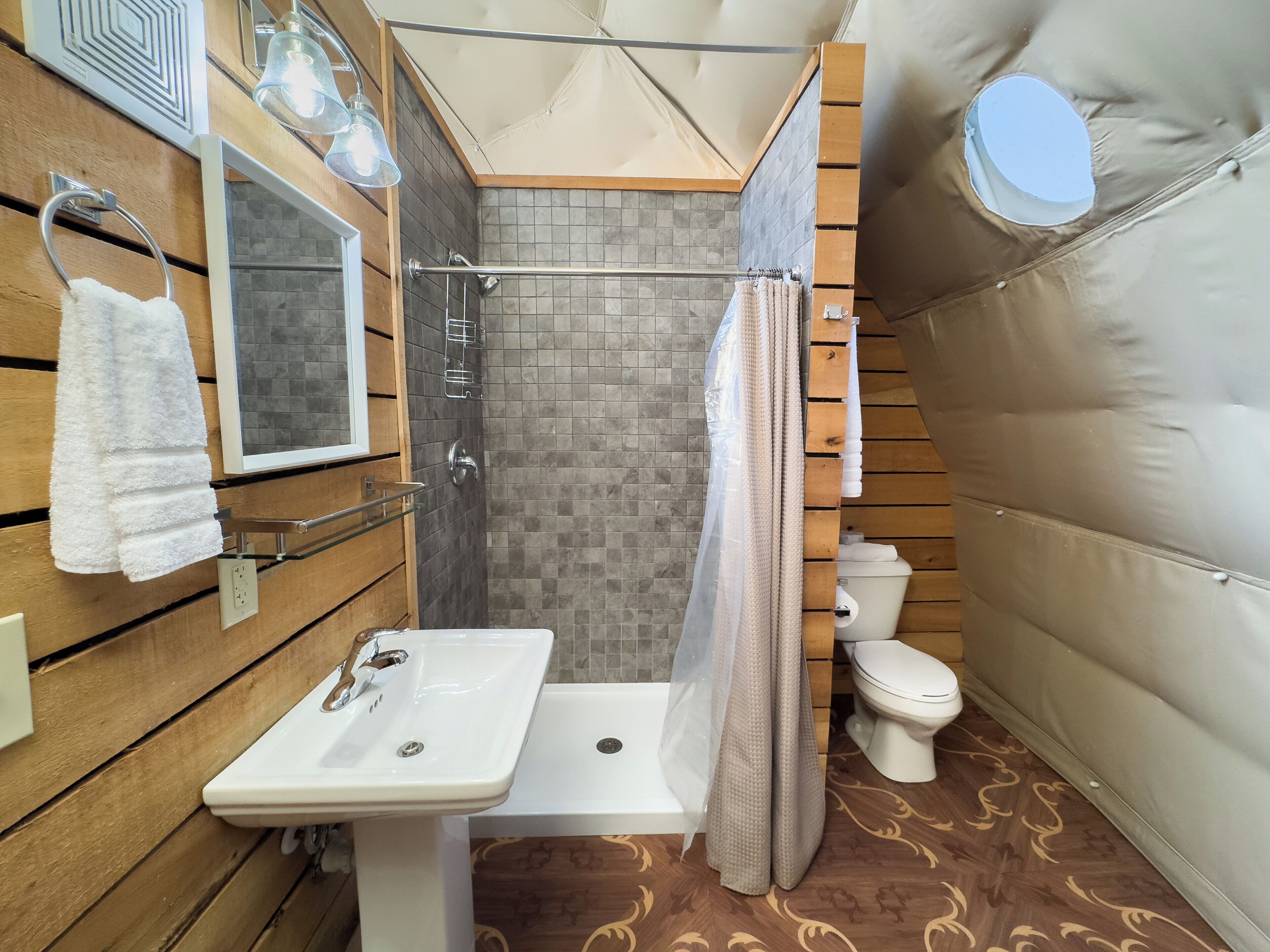 Un baño con pared de madera, un lavamanos blanco, ducha con puerta de cristal y un inodoro.