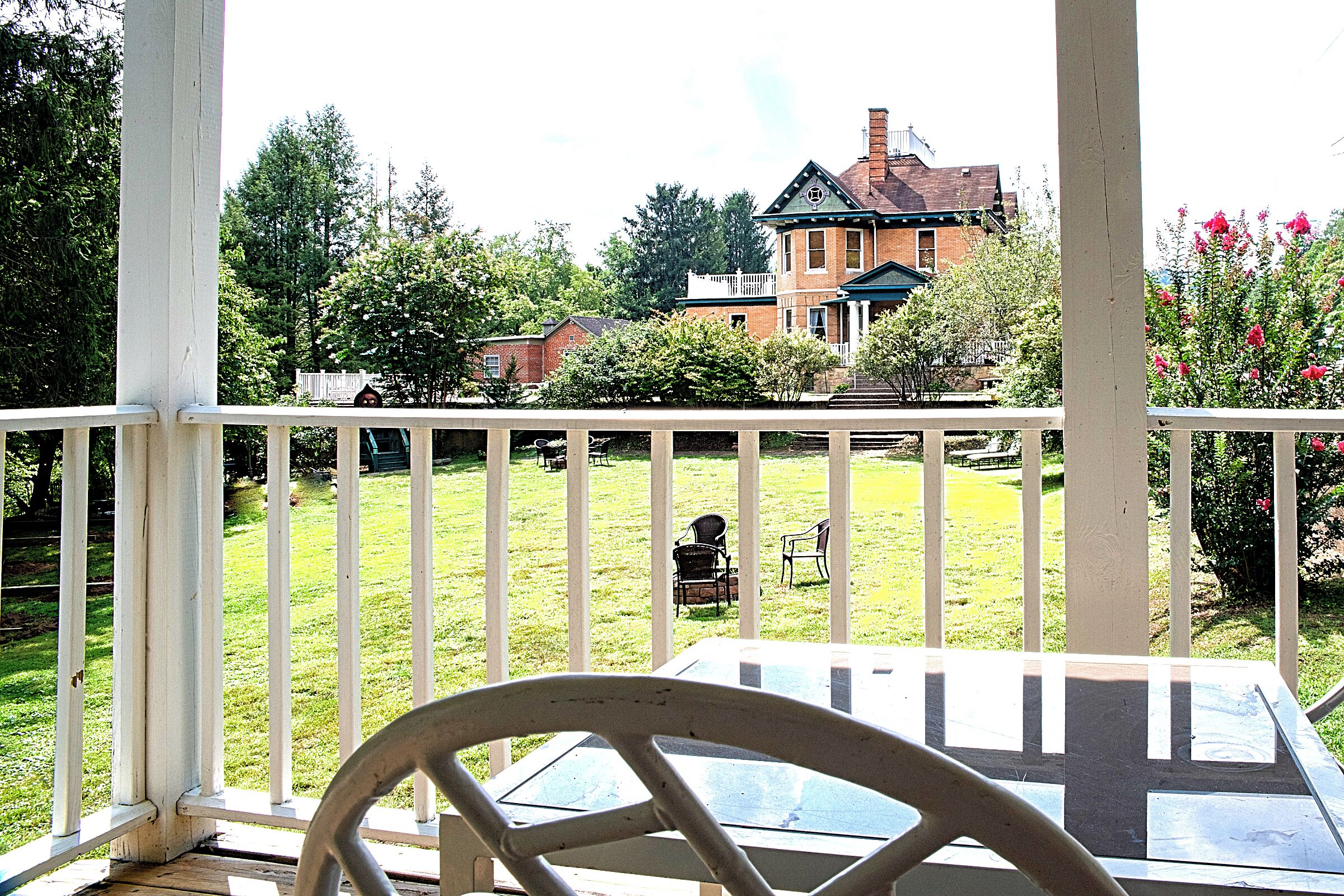 Un espace extérieur abrité, doté d’une table et de chaises, d’une rambarde blanche et offrant une vue sur une maison et une pelouse.