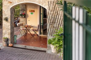 Een terras met een stenen boog, een tafel, stoelen en een bord dat een restaurant of café aangeeft.