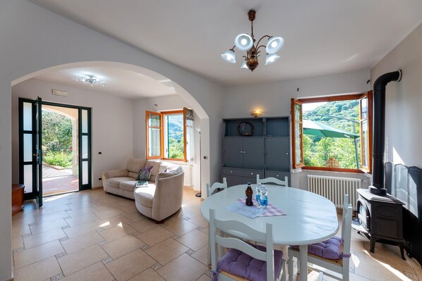 Un vaste espace de vie comprenant un canapé, une table à manger et offrant une vue sur la verdure grâce à de grandes fenêtres.