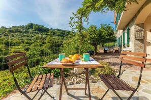 Un espace extérieur aménagé pour prendre les repas, avec une table dressée pour le petit-déjeuner, entouré de murs en pierre et de verdure.