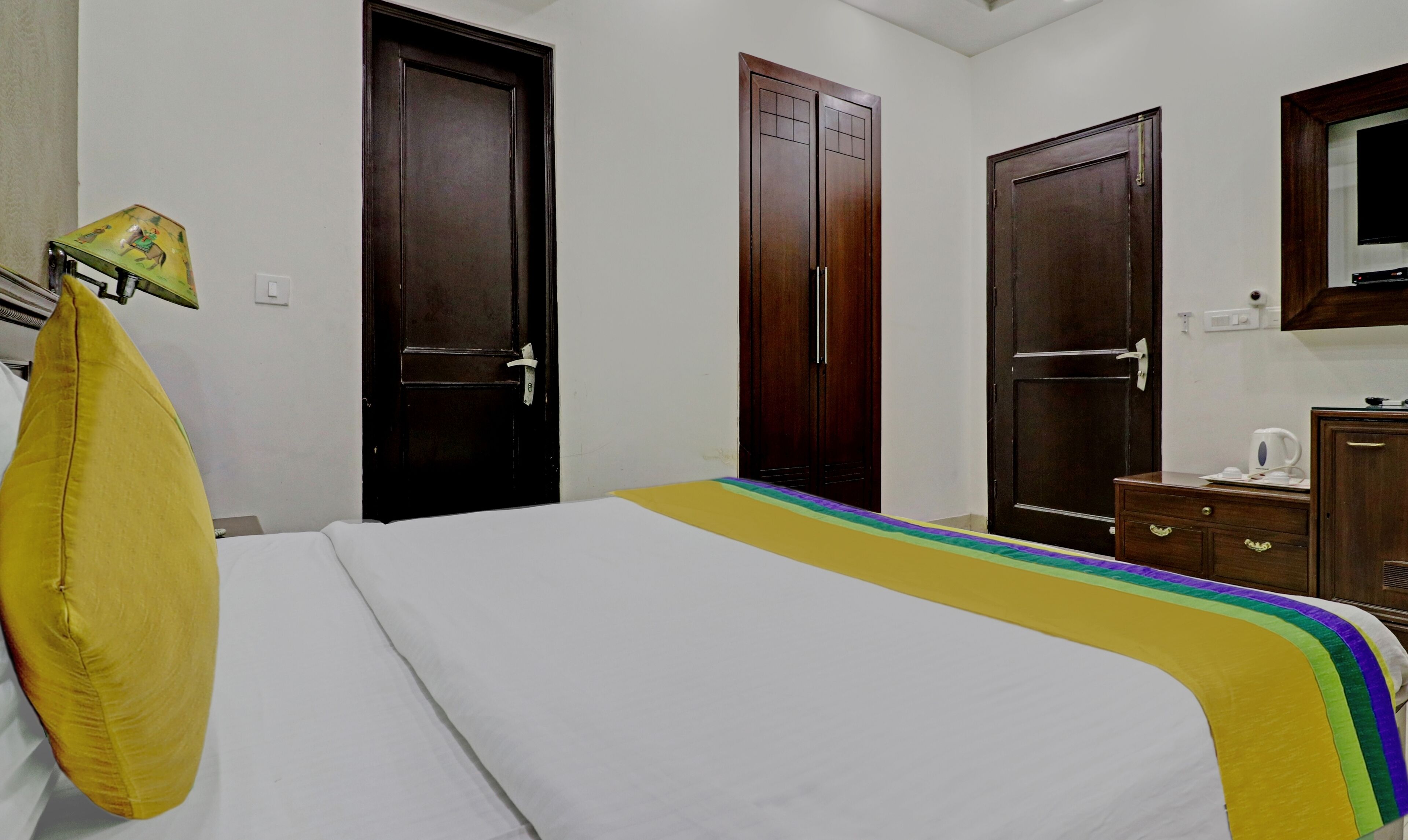 A hotel room with a bed, two wooden doors, a small cabinet, and a television on the wall.