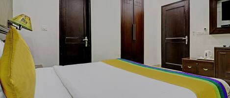 A hotel room with a bed, two wooden doors, a small cabinet, and a television on the wall.