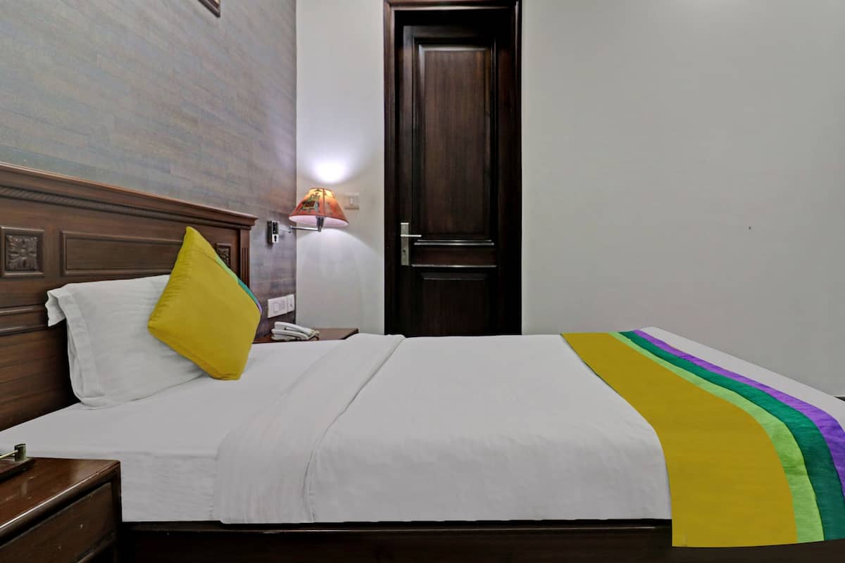 Een hotelkamer met een bed, een nachtkastje, een lamp en een deur.