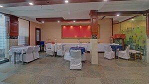 A conference room with multiple tables and chairs, a large red wall panel, and a tiled floor. - Itsy Hotels Hamlets Stay (Noida)