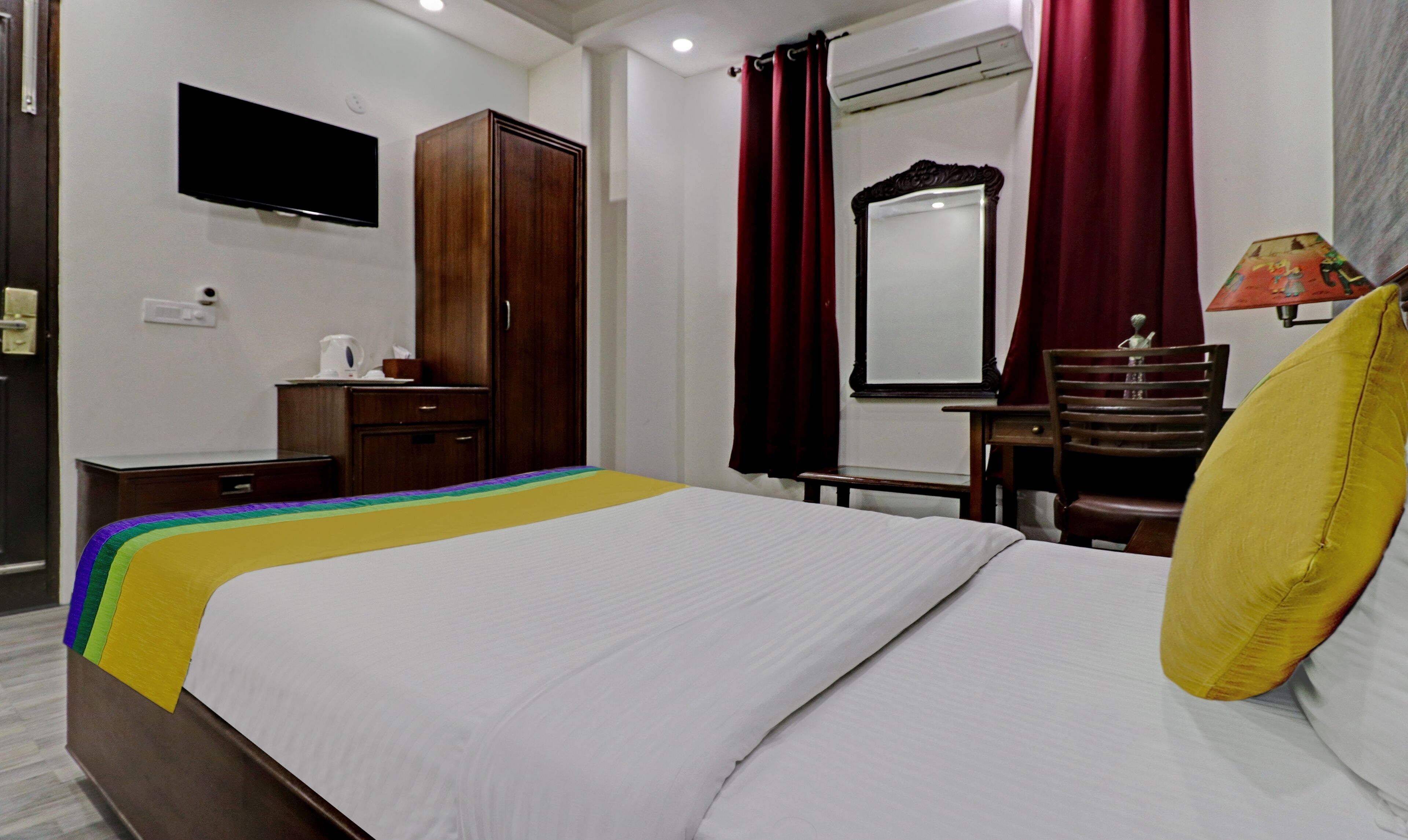 A hotel room with a bed, a television, a wardrobe, a desk, a chair, and a mirror.