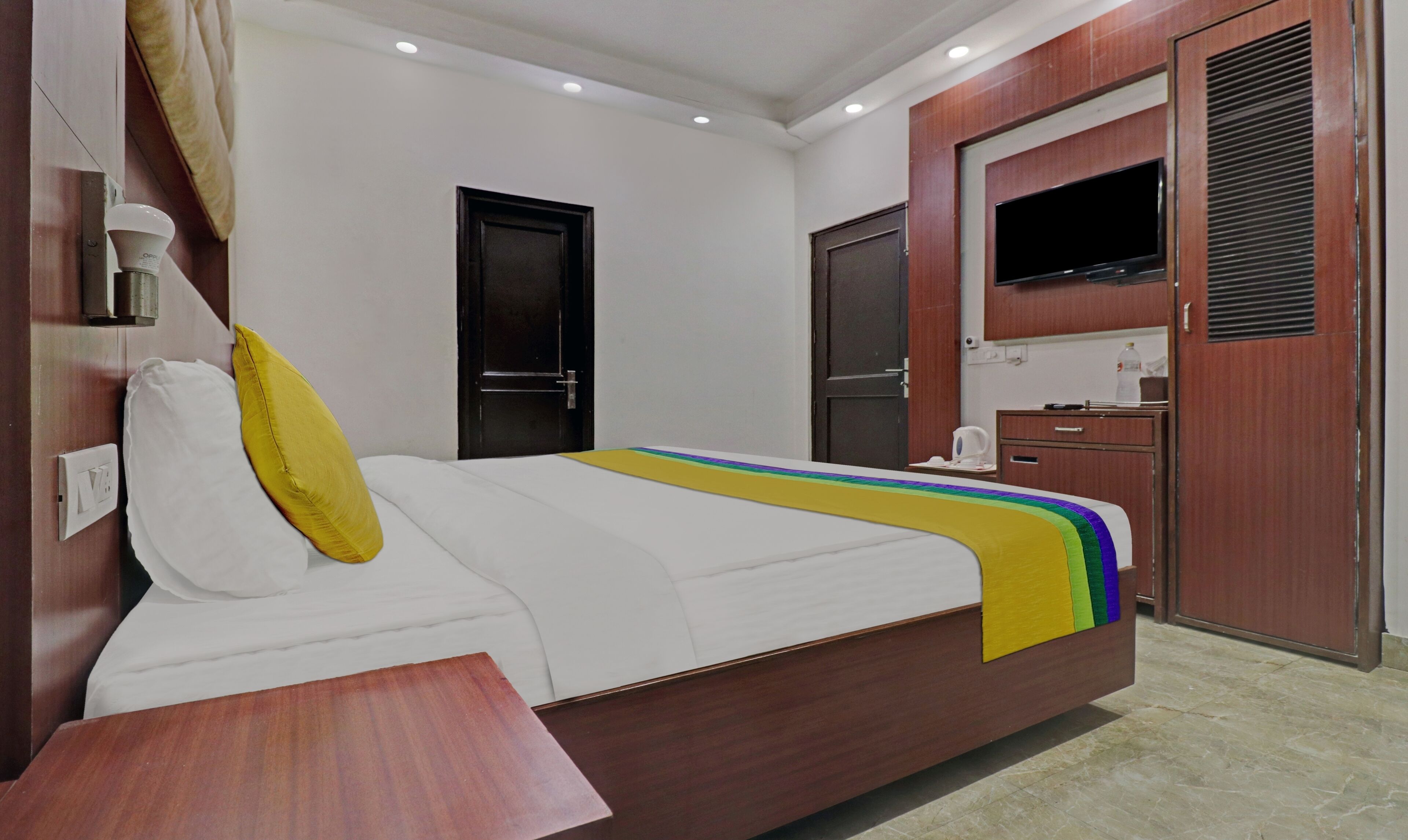 A hotel room with a bed, a bedside table, a TV, a wardrobe, and a bathroom door.