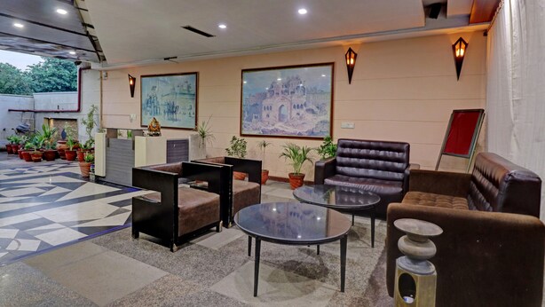 A hotel lobby with a checkered floor, seating area with sofas and a glass table, potted plants, and two large paintings on the walls. - Itsy Hotels Hamlets Stay (Noida)