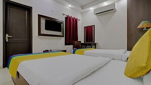 A hotel room with two beds, a TV, an air conditioner, and a desk. - Itsy Hotels Hamlets Stay (Noida)