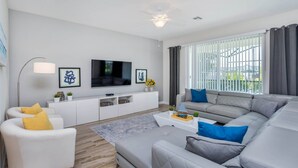 A modern living room with a grey sofa, white armchair, and a flat-screen TV mounted on the wall.
