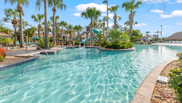 Una piscina cristalina con palmeras, un tobogán y sillas de descanso.