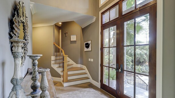 Un escalier menant à un deuxième étage, une grande porte en bois avec des panneaux de verre et un élément décoratif fixé au mur.