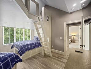 A bedroom with a loft bed, a wooden desk, and a view of the outdoors through large windows.