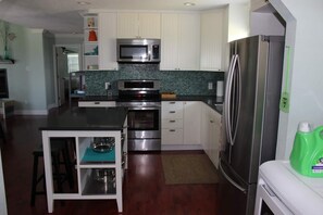A modern kitchen with white cabinets, stainless steel appliances, and a green backsplash.