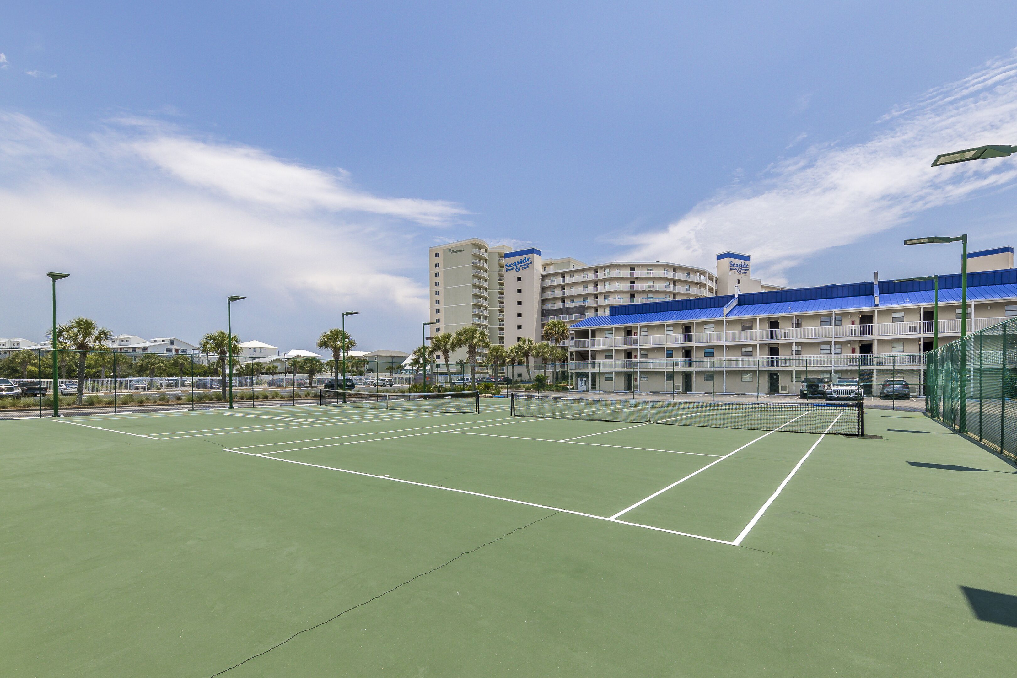Un court de tennis avec un filet, entouré d’une clôture, et des bâtiments en arrière-plan.