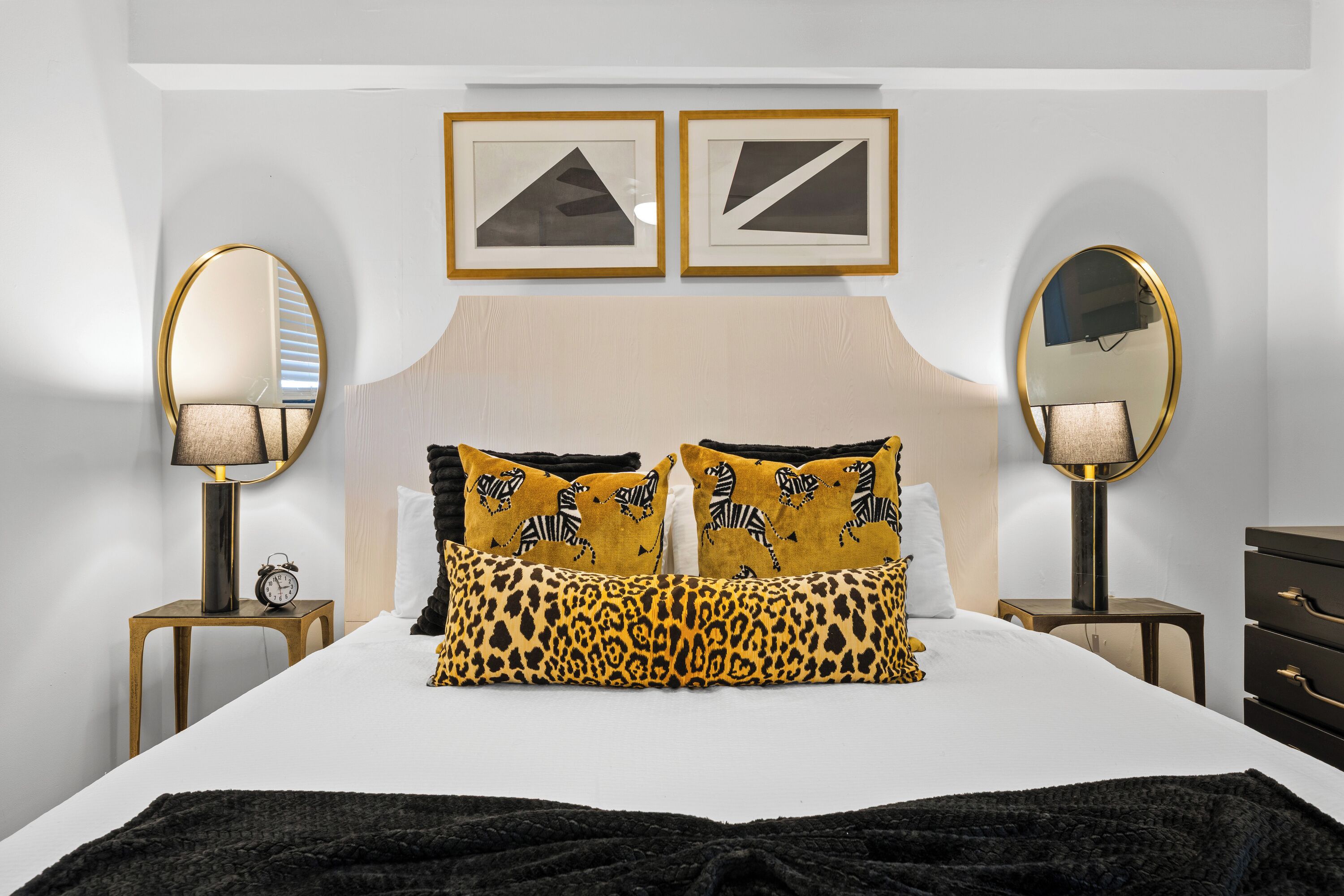 Een slaapkamer met een bed, twee nachtkastjes, een kaptafel en twee spiegels aan de muur.