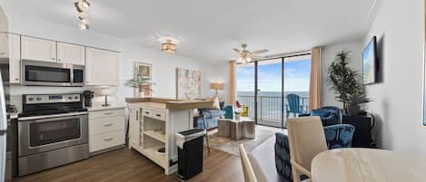 A modern kitchen with stainless steel appliances, a dining area with a table and chairs, and a balcony with a view.