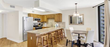 A modern kitchen with wooden cabinets, a stainless steel refrigerator, and a bar area with stools.