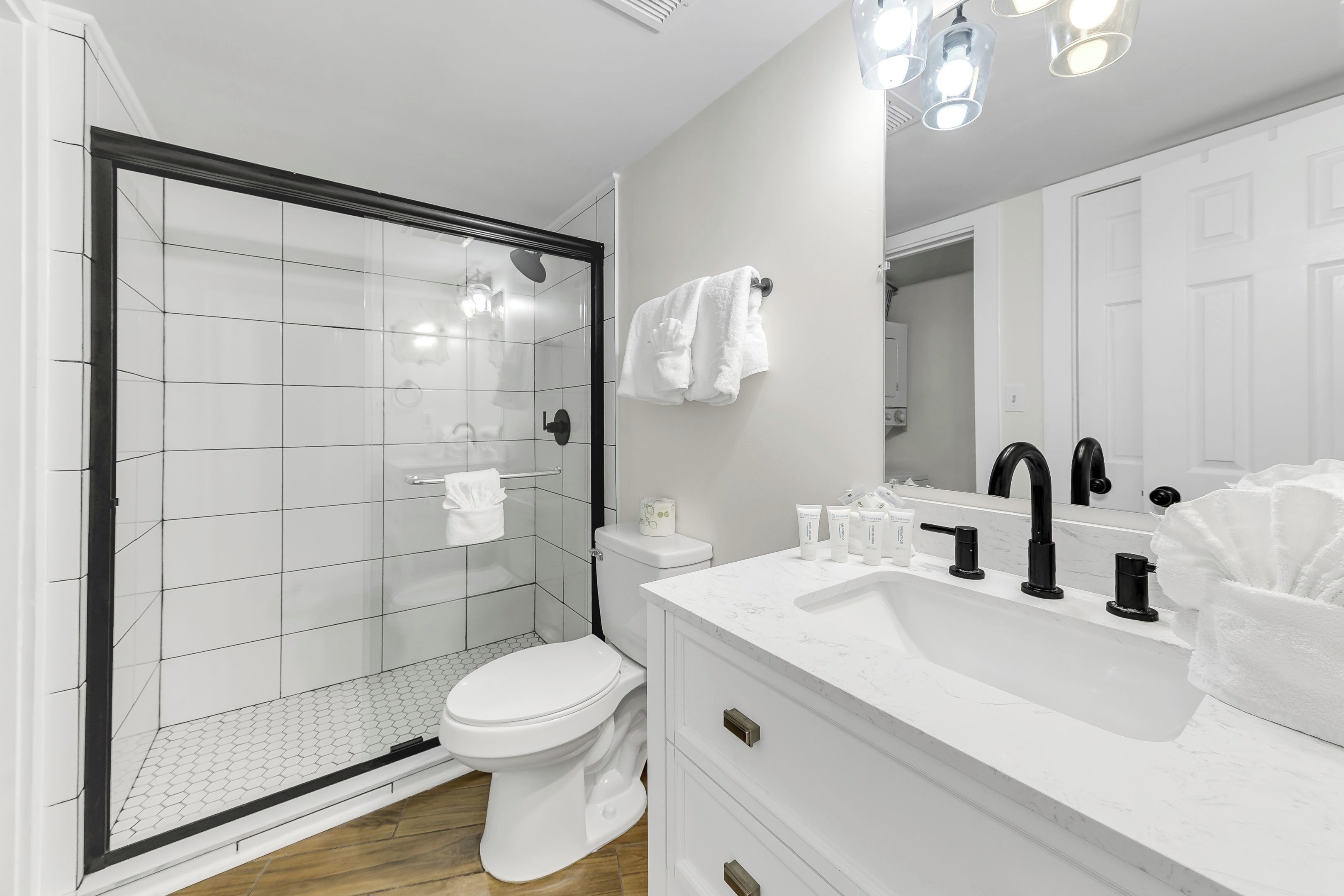 A modern bathroom with a glass-enclosed shower, a white toilet, and a white vanity with black faucets.