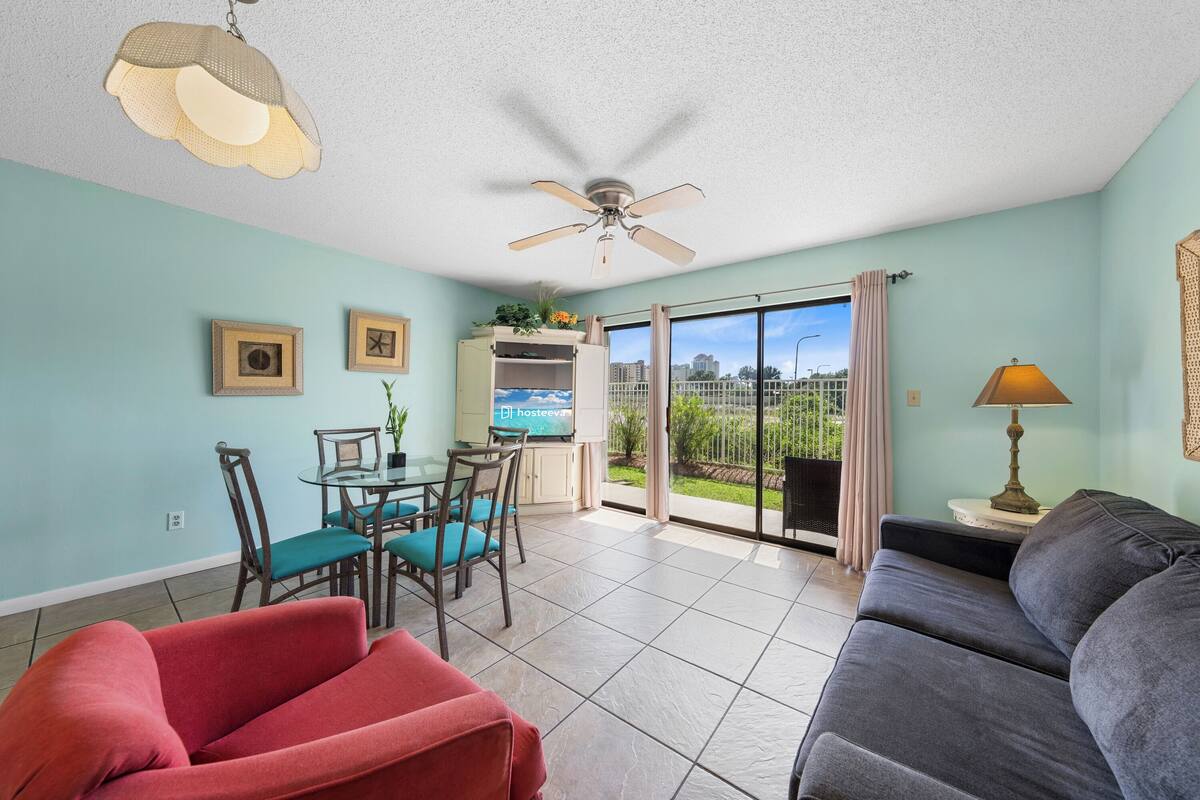 A spacious living area with a dining table, chairs, a sofa, a ceiling fan, and a view through a sliding glass door.