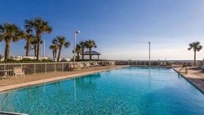 A clear blue pool with lounge chairs and palm trees, surrounded by a fence and a view of the ocean. - Seaside Beach & Racquet Condos (Orange Beach)