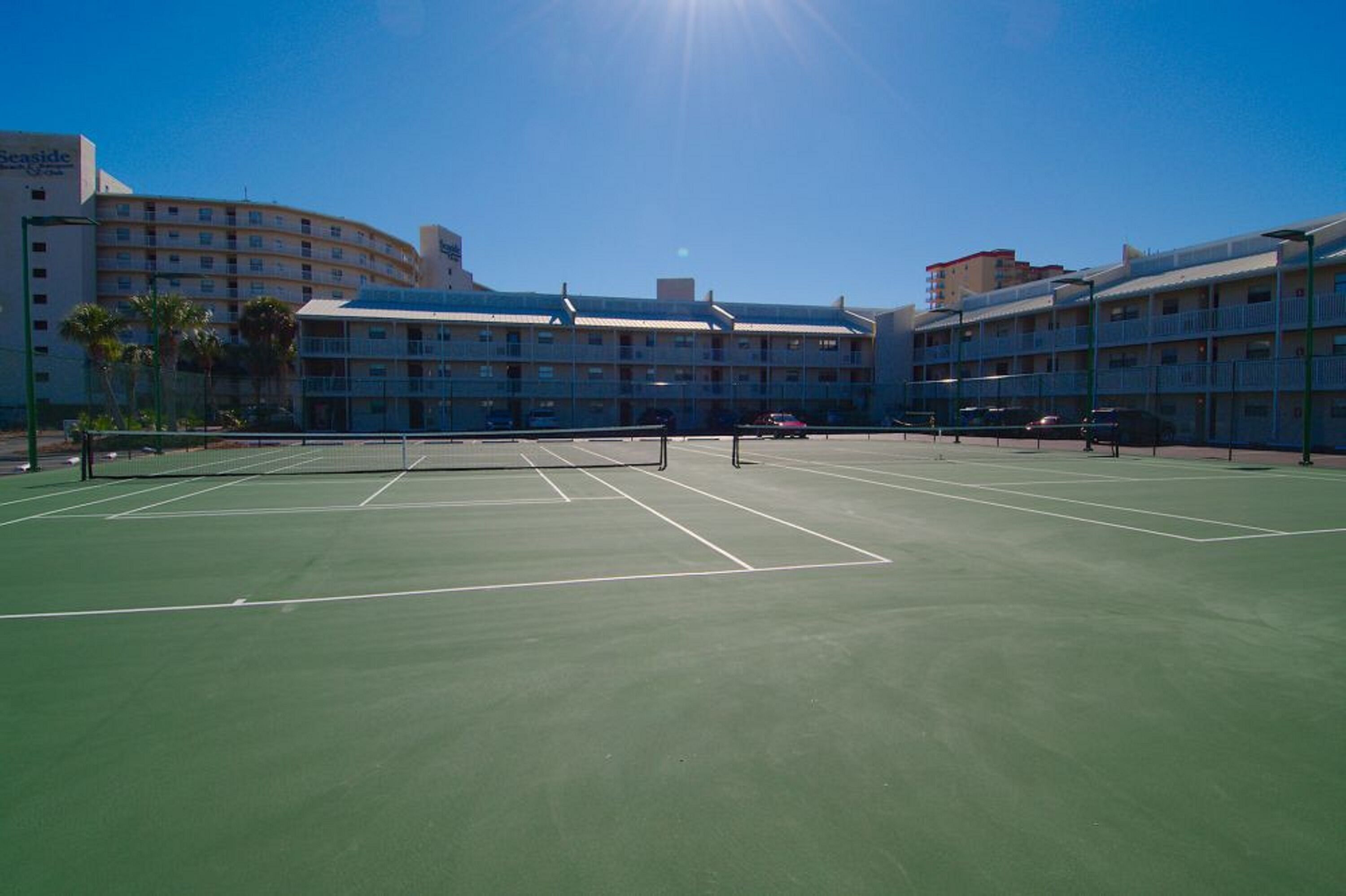 Un court de tennis avec un filet au centre, entouré de bâtiments d’hôtel dotés de balcons.