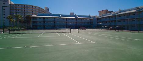 Un court de tennis avec un filet au centre, entouré de bâtiments d’hôtel dotés de balcons.