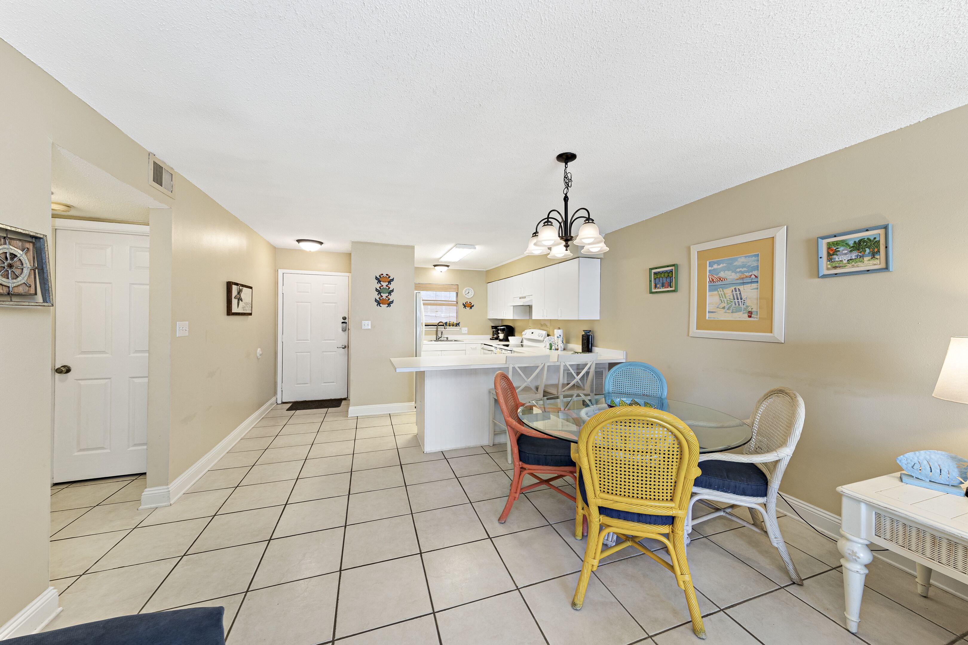 A compact kitchen with white cabinets, a central island, and a dining area with wicker chairs.