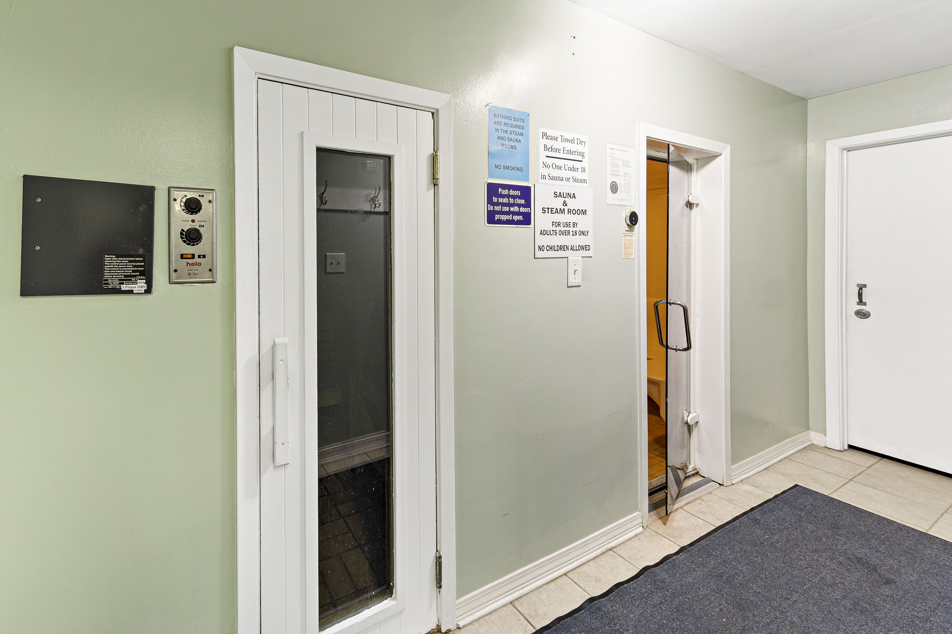 A hallway with a sauna room door, a steam room door, and a towel drying area.