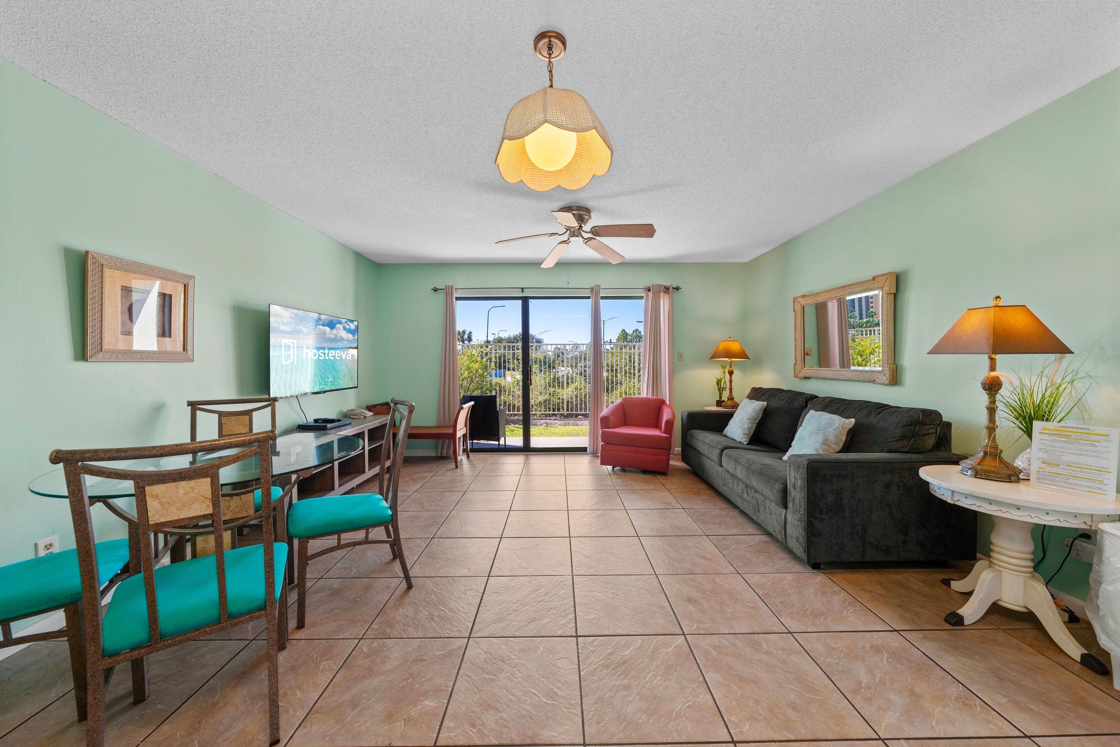 A living room with a dining area, a sofa, a red chair, a ceiling fan, and a television.