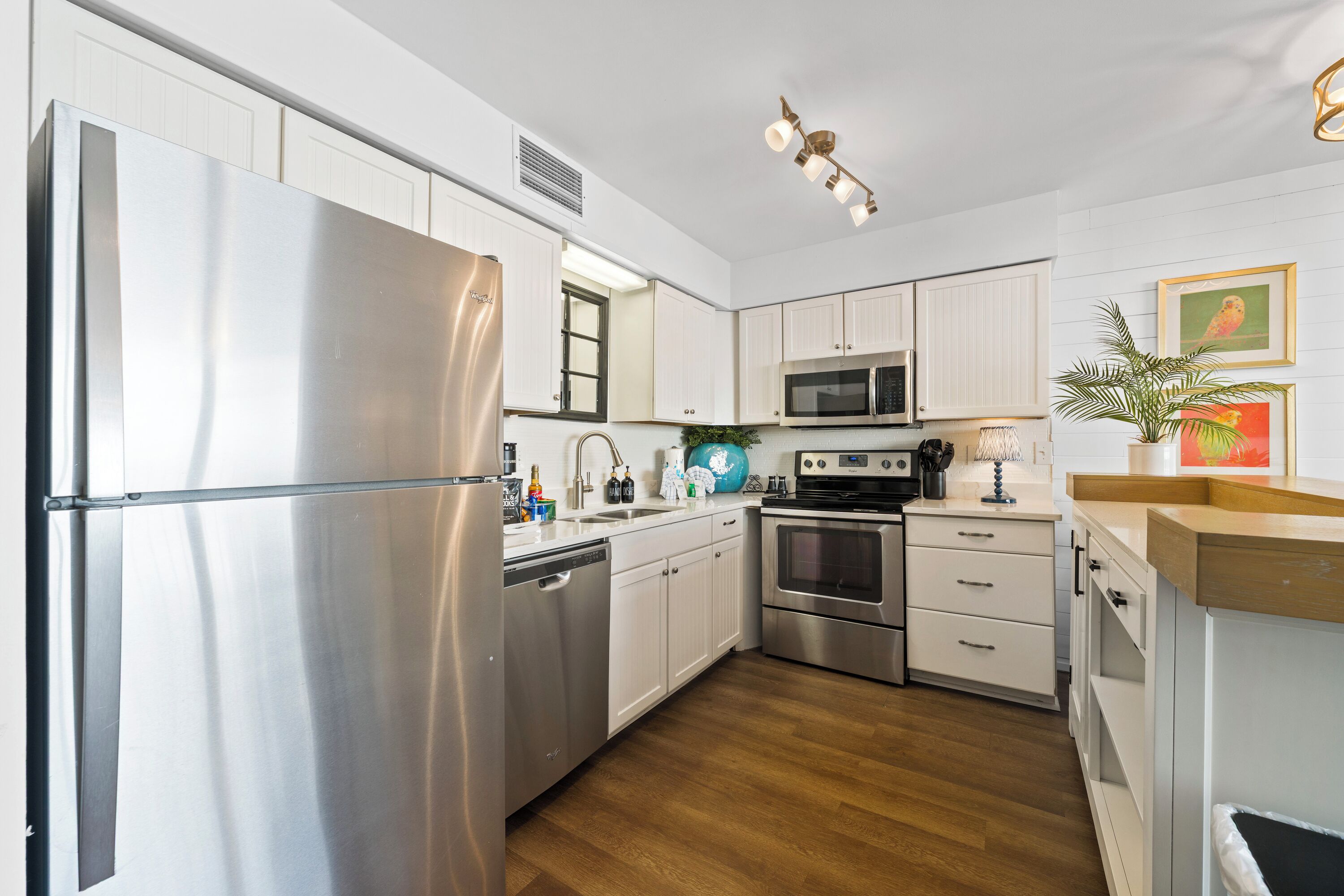 A modern kitchen with stainless steel appliances, white cabinetry, and wooden flooring.