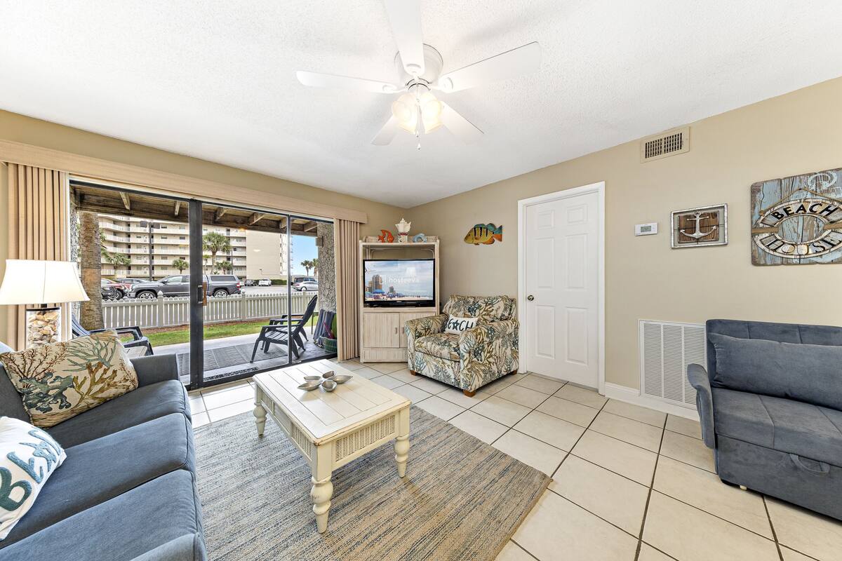 A living room with a television, a ceiling fan, and a view of the outside.
