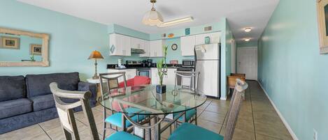 A compact living space with a kitchenette, a dining area with a glass table, and a sofa.