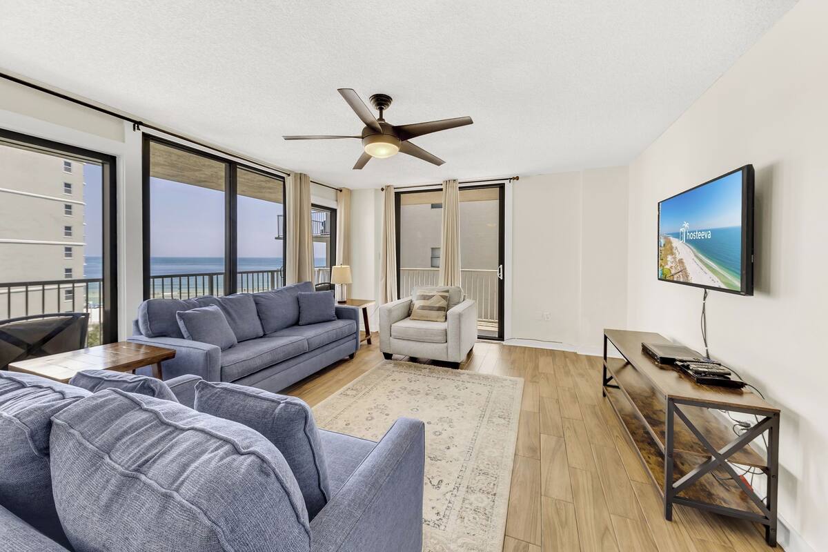 A modern living room with a large sofa, a smaller armchair, a coffee table, and a TV mounted on the wall.