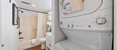 A compact bathroom with a bathtub, toilet, and a white washing machine with control panel.