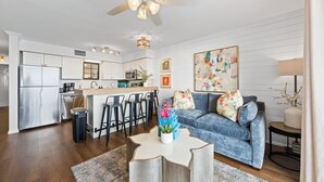 A modern kitchen with white cabinetry, a stainless steel refrigerator, and a dining area with bar stools. - Seaside Beach & Racquet Condos (Orange Beach)