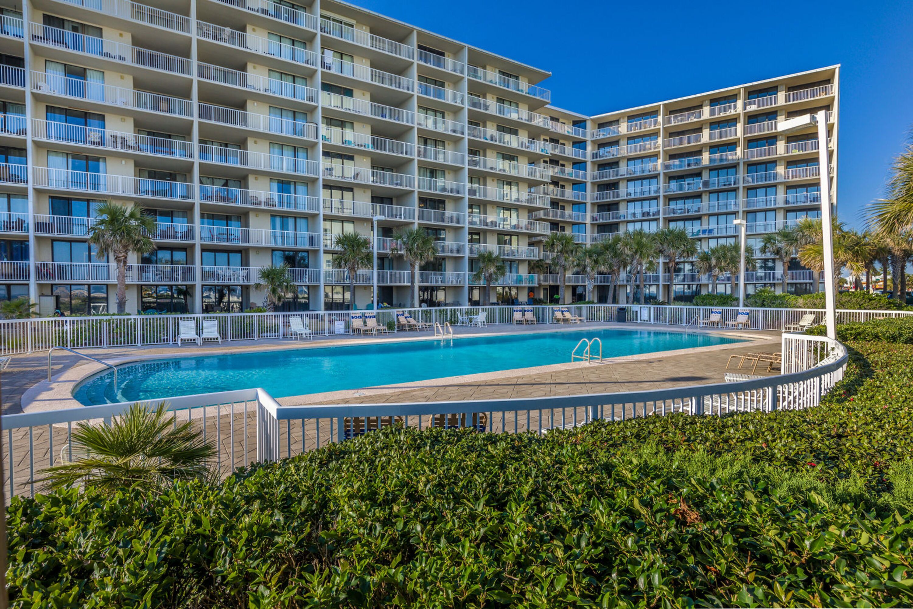 A hotel with a large pool surrounded by palm trees and a white fence.