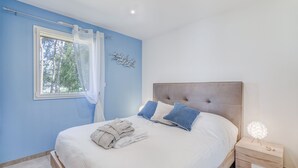 Et soveværelse med seng, et natbord, et vindue med udsigt til træer og en loftlampe.