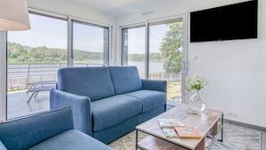 En moderne stue med en blå sofa, et træ sofabord og et TV ophængt på væggen.