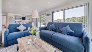A modern living room with two blue sofas, a wooden coffee table, and a view of the outdoors. - Les Roseaux - Vue sur le lac avec jacuzzi (Sanchey)