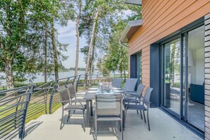 Een buiten eethoek met een tafel voor vier personen, met uitzicht op een waterpartij, met een modern gebouw en bomen op de achtergrond.