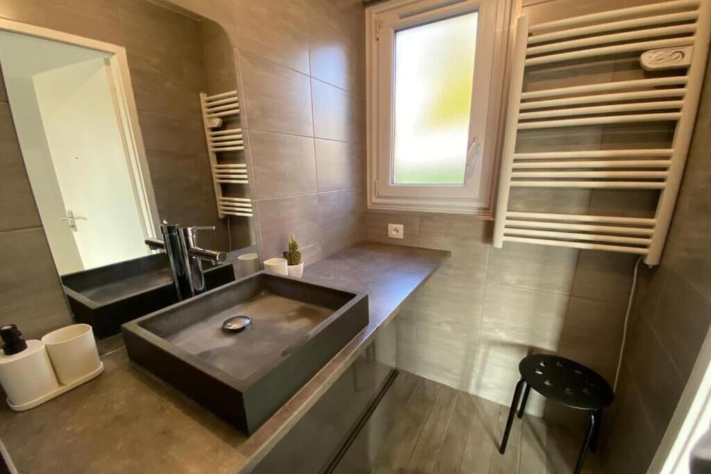 Ein modernes Badezimmer mit einem großen Spiegel, einem rechteckigen Waschbecken und einem Fenster mit Jalousien.